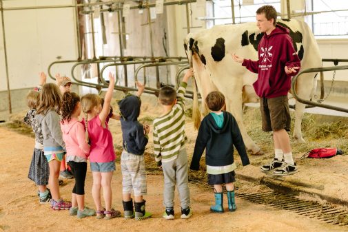 a group of kids standing in a milking barn with hands raised for questions