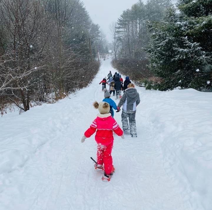 A group of kids snowshoe up a long plath as it lightly snows
