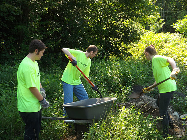 Three Young Adults in matching neon shirts working with some gravel.